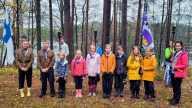 Aikuisia ja lapsia rivissä partiohuivit kaulalla Suomenlipun ja Metsänkkävijöiden lipun sekä palavien soihtujen ollessa taustalla.